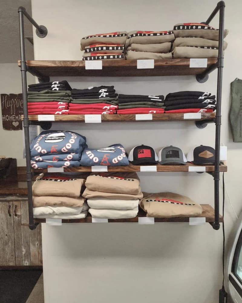 Shelf of folded Ashton Farms and Ashton's Burger Barn branded t-shirts and trucker hats